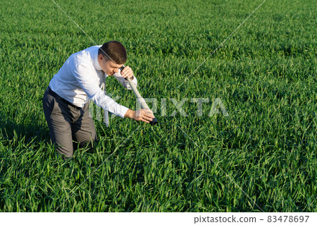 businessman poses with a spyglass, he looks into the grass and looks for something, green grass and blue sky as background 83478697