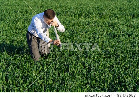businessman poses with a spyglass, he looks into the grass and looks for something, green grass and blue sky as background 83478698