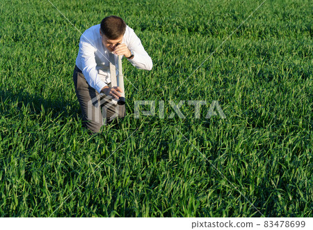 businessman poses with a spyglass, he looks into the grass and looks for something, green grass and blue sky as background businessman poses with a spyglass, he looks into the grass and looks for something, green grass and blue sky as background 83478699