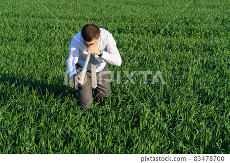 businessman poses with a spyglass, he looks into the grass and looks for something, green grass and blue sky as background businessman poses with a spyglass, he looks into the grass and looks for something, green grass and blue sky as background 83478700