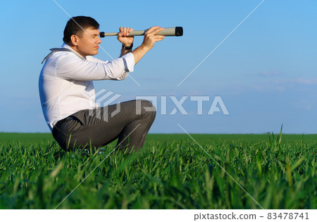 businessman poses with a spyglass in a green field, he looks an idea or something, business concept, green grass and blue sky as background businessman poses with a spyglass in a green field, he looks an idea or something, business concept, green grass and blue sky as background 83478741