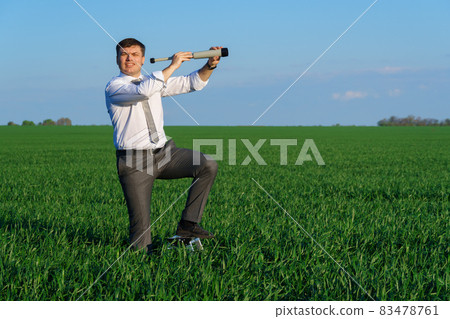 businessman poses with a spyglass in a green field, he looks an idea or something, business concept, green grass and blue sky as background 83478761