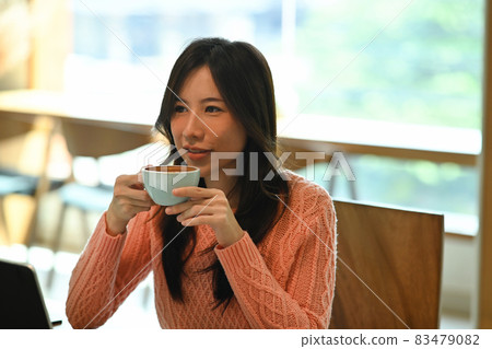 Young asian woman in sweater drinking hot coffee. Young asian woman in sweater drinking hot coffee. 83479082