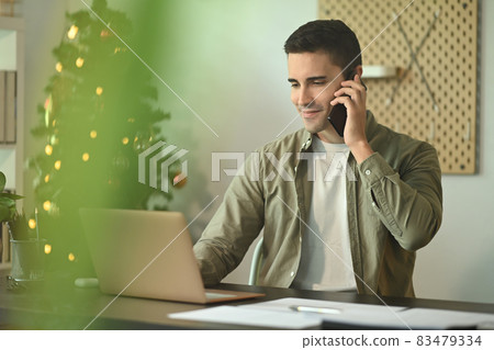 Smiling handsome man using laptop computer and talking on mobile phone. Smiling handsome man using laptop computer and talking on mobile phone. 83479334