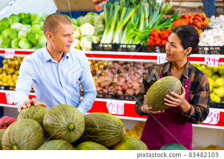 Saleswoman helping male buyer to choose melon in store Saleswoman helping male buyer to choose melon in store 83482103