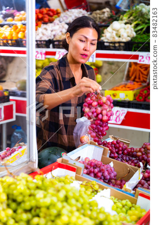 Asian woman choosing ripe grapes in greengrocery store 83482163