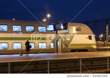 KOUVOLA, FINLAND - NOVEMBER 8, 2018: Long exposure photo. Train on the station at night. Blurred woman with travel bag staying on the platform. KOUVOLA, FINLAND - NOVEMBER 8, 2018: Long exposure photo. Train on the station at night. Blurred woman with travel bag staying on the platform. 83482350