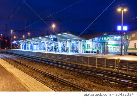 KOUVOLA, FINLAND - NOVEMBER 8, 2018: Long exposure photo. Train on the station at night. Blurred passengers with travel bags walking and staying on the platform. 83482354