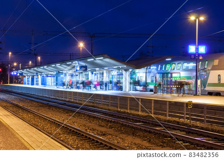 KOUVOLA, FINLAND - NOVEMBER 8, 2018: Long exposure photo. Train on the station at night. Blurred passengers with travel bags walking and staying on the platform. 83482356