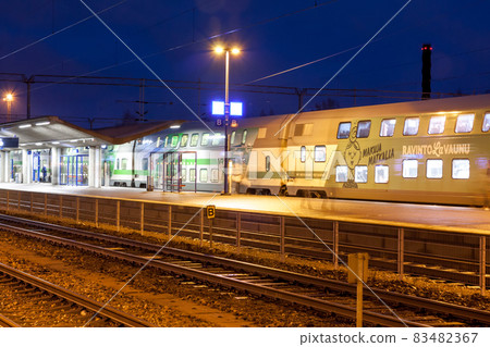 KOUVOLA, FINLAND - NOVEMBER 8, 2018: Long exposure photo. Train on the station at night. Blurred passengers with travel bags walking and staying on the platform. 83482367