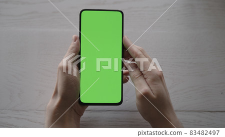 Man using phone with green screen on white oak table 83482497
