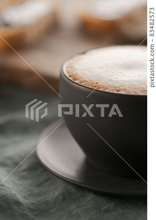 Cappuccino in black cup with ciabatta slices with chocolate spread on background Cappuccino in black cup with ciabatta slices with chocolate spread on background 83482573