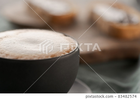 Cappuccino in black cup with ciabatta slices with chocolate spread on background Cappuccino in black cup with ciabatta slices with chocolate spread on background 83482574