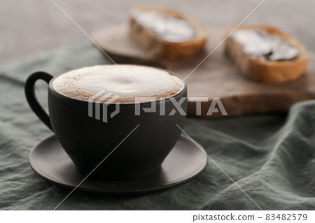 Cappuccino in black cup with ciabatta slices with chocolate spread on background Cappuccino in black cup with ciabatta slices with chocolate spread on background 83482579