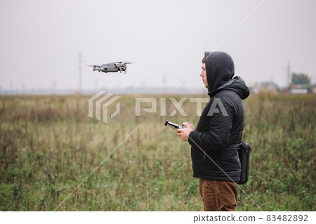 Portrait of drone operator flying aircraft quadcopter near the forest. 83482892