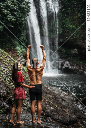 Couple at the waterfall, rear view. Honeymoon trip. Couple on vacation in Bali. A couple in love travels the world. Vacation on the island of Bali. Happy couple close up. Tourists at the waterfall Couple at the waterfall, rear view. Honeymoon trip. Couple on vacation in Bali. A couple in love travels the world. Vacation on the island of Bali. Happy couple close up. Tourists at the waterfall 83483101