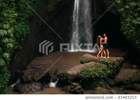 Lovers at the waterfall. Couple admiring a beautiful waterfall in Indonesia. Couple on vacation in Bali. Honeymoon trip. The couple is traveling in Asia. Vacation in Bali. Copying a space 83483253