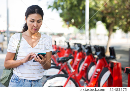 Woman with smartphone beside bike share station Woman with smartphone beside bike share station 83483375