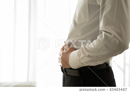 A man in a suit is putting his hand on his abdomen 83483487