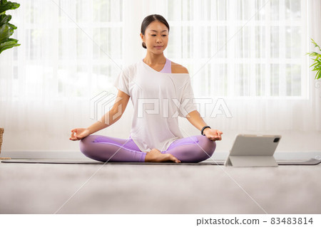 Morning yoga with an Asian woman, sitting in Easy position, Sukhasana posture, and meditating online. 83483814