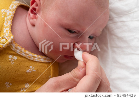 Cleaning newborn nose from boogers with a cotton swab 83484429