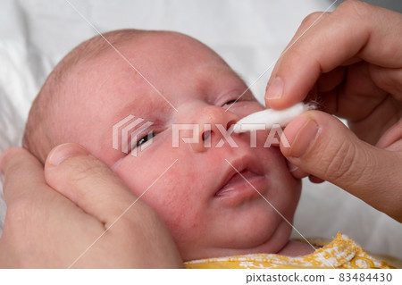 Cleaning newborn nose from boogers with a cotton swab 83484430