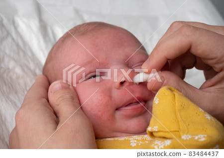 Cleaning newborn nose from boogers with a cotton swab 83484437