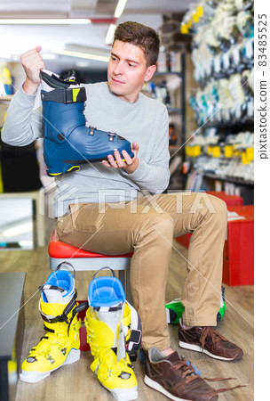 Guy is trying on stylish boots for skiing in sport shop. 83485525