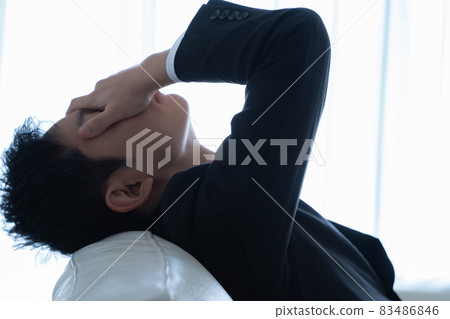 A businessman lying on the sofa and holding his face 83486846