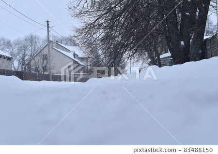 Rural road covered with snow and roofs of residential buildings. 83488150