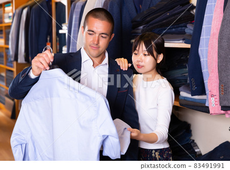 Female shopping assistant offering various shirts in mens cloths store 83491991