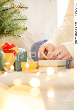 woman hand tieding ribbon new year gift box and decorate christmas tree woman hand tieding ribbon new year gift box and decorate christmas tree 83492737