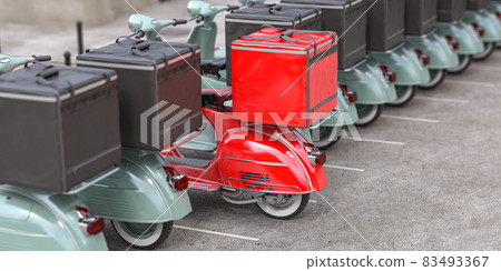 Red delivery scooter with delivery bag in a row of mopeds of grey color. Fast express delivery concept. Red delivery scooter with delivery bag in a row of mopeds of grey color. Fast express delivery concept. 83493367