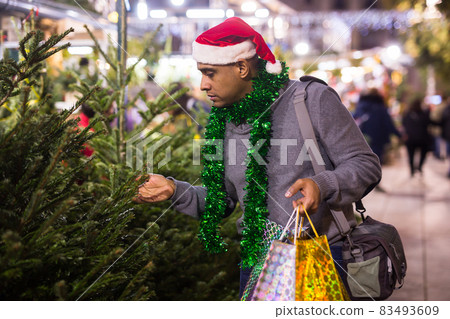 Positive man buying Christmas tree and toys at Christmas Fair Positive man buying Christmas tree and toys at Christmas Fair 83493609