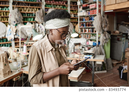African young dressmaker working online on digital tablet in the workshop, she examining new sketches online African young dressmaker working online on digital tablet in the workshop, she examining new sketches online 83493774