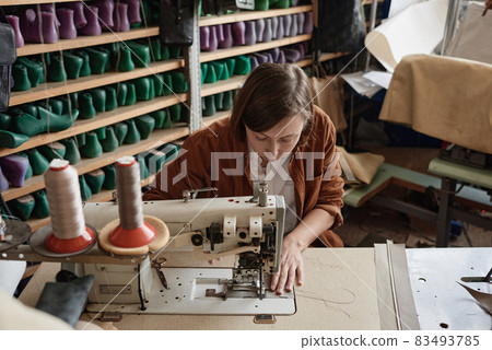 Shoemaker sitting at the table and using sewing machine in her work, she sewing new shoes 83493785