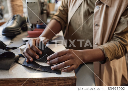 Close-up of tailor sitting at the table and examining the pieces of leather during her work in the workshop 83493902
