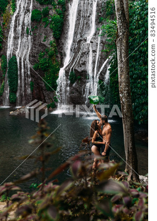 Beautiful couple at a waterfall in Indonesia. A couple in love travels around the island of Bali. A man and a woman kiss at the waterfall. Travel to Asia. Honeymoon trip. Tourists at the waterfall 83494516