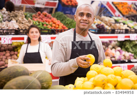 Friendly seller posing with yellow lemons in local supermarket Friendly seller posing with yellow lemons in local supermarket 83494958