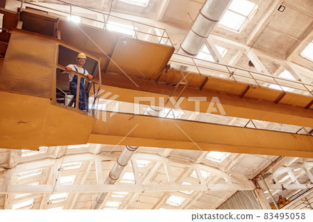Joyful worker standing in operator cabin of overhead crane Joyful worker standing in operator cabin of overhead crane 83495058