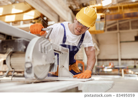 Smiling male worker using sawing machine in workshop 83495059