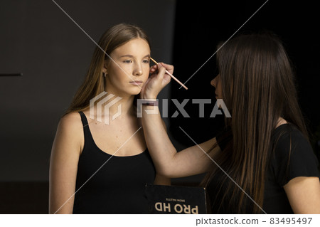 Makeup artist doing a eyebrows makeup on a beautiful woman face. Hand of make-up master is painting eyebrow of young beauty model girl. Make up in process. Makeup artist doing a eyebrows makeup on a beautiful woman face. Hand of make-up master is painting eyebrow of young beauty model girl. Make up in process. 83495497