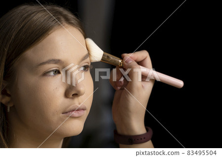 Close up face of beautiful young woman getting powder on her cheek with a brush. Professional makeup artist. Close up face of beautiful young woman getting powder on her cheek with a brush. Professional makeup artist. 83495504