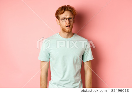 Portrait of handsome redhead man in glasses looking confused, open mouth and stare at camera, cant understand nothing, standing over pink background Portrait of handsome redhead man in glasses looking confused, open mouth and stare at camera, cant understand nothing, standing over pink background 83496018
