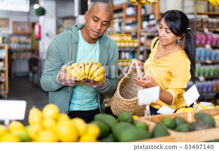 Hispanic married couple choosing bananas in grocery store 83497140