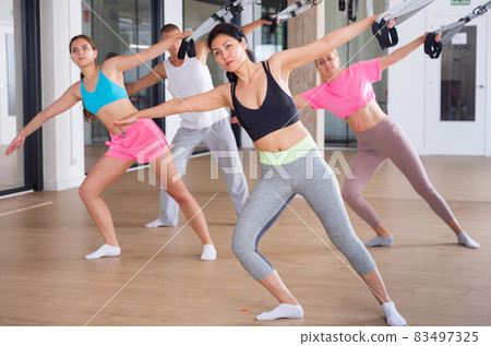 Sports people perform an exercise for stretching muscles using a special suspended structure 83497325