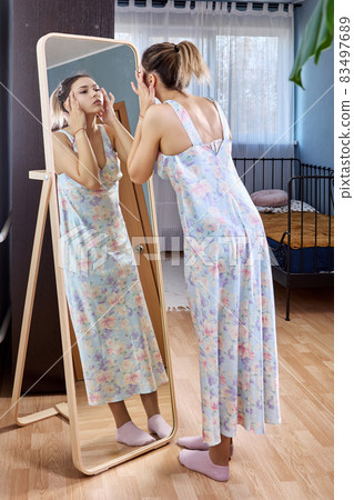 Large full length standing mirror and woman in dress is looking in it. 83497689