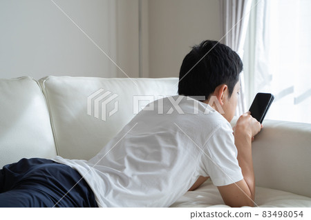 A man lying on the sofa and playing with his smartphone A man lying on the sofa and playing with his smartphone 83498054