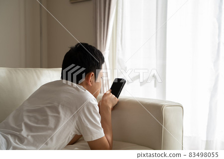 A man lying on the sofa and playing with his smartphone A man lying on the sofa and playing with his smartphone 83498055