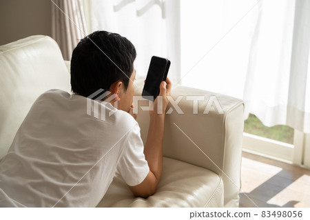 A man lying on the sofa and playing with his smartphone A man lying on the sofa and playing with his smartphone 83498056